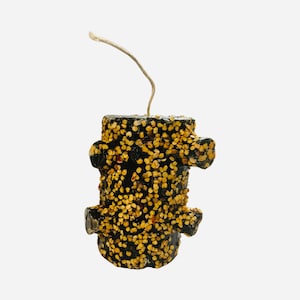 May include: A black candle shaped like a tree trunk with a brown wick. The candle is covered in small, golden-colored dots.