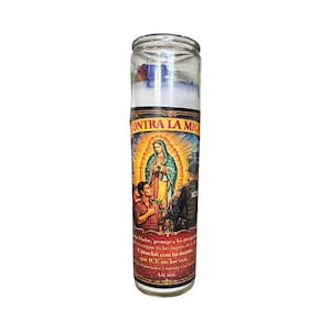 May include: A glass candle with a label featuring an illustration of the Virgin Mary, two men, and two law enforcement officers. The label has the text "CONTRA LA MIG" and other Spanish text. The candle is filled with white wax and has a clear glass exterior.