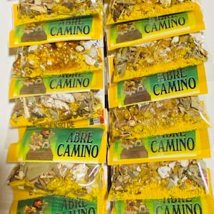 Puede incluir: Una pila de diez pequeños paquetes amarillos y verdes que contienen hierbas y cristales sueltos. Cada paquete tiene una etiqueta que dice "Legitimo Sahumerio e Incienso de Abre Camino".