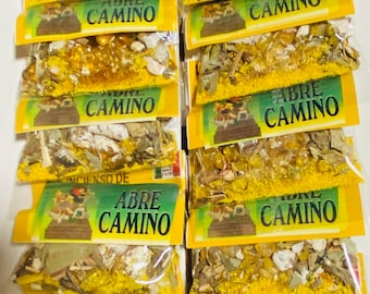 May include: A stack of ten small yellow and green packages containing loose herbs and crystals. Each package has a label that reads "Legitimo Sahumerio e Incienso de Abre Camino".