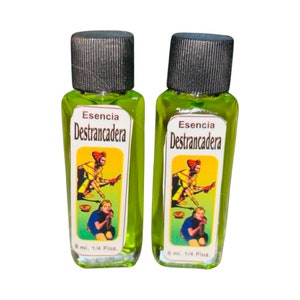 May include: Two small green glass bottles with black caps. Each bottle has a yellow label with the text "Esencia Destrancadera" and a colorful illustration of a person. The bottles contain 8 ml or 1/4 fl oz of liquid.