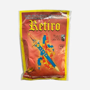 May include: A clear plastic bag with a red background and yellow borders. The bag features the word "Retiro" in gold lettering and a colorful illustration of a sword and ribbons. Text includes "Bath of Aromatic Plants Delightfully".
