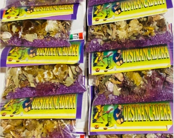 May include: A stack of small, clear plastic bags filled with dried herbs and purple crystals. Each bag has a yellow label with the text "Legitimo Sahumerio e Incienso de Destrancadera" printed on it.