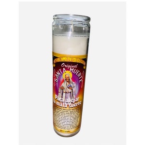 May include: White candle in a glass jar with a colorful label featuring an image of Santa Muerte, a skeletal figure in a robe, holding a scale and a globe. The label reads "Original Santa Muerte Para alejar la mala suerte".