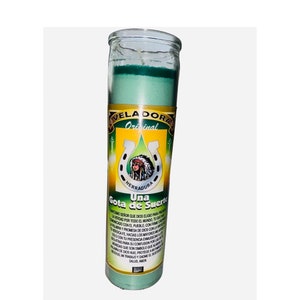 May include: A green glass candle with a yellow label that reads "VELADORA Original HERRADURA Una Gota de Suerto". The label also includes a drawing of a horseshoe with a Native American woman inside. The text on the label reads: "MOONGSENOR QUE DIOS ELIGIO PARA PROTEGER LA MERCAD POR TODO EL MUNDO, TU CREES EN LA PALABRA CON EL PUEBLO, CONFIA EN MI VERDICA Y HAZ LAS COSAS CON LA MAYOR FE, SOLO CON TU PRESENCIA EMPOBRECE MI DOLOR PARA QUE SUSEN CONFUSIONES LAS COLATAS QUE SON SIMBOLO DE LA FAMILIA, MOONGDE DIOS HUDO, PROTEGE A MI HUJO, MI TRABAJO Y DAME EL SUERTEN SALUD, AMEN"