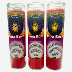 May include: Three red glass candle jars with a woman's face wearing a yellow mask on the front. The text on the candle jars reads "Veladora Original Tapa Boca" and "Oh! Espiritus Justicieros Tapen La Boca De: De Todo Aquel Hombre O Mujer Que Trate De Hostilizarme, Dañarme O Perjudicarne Con Malas Lenguas O Chismes. Oh! Espiritus Justicieros, Tapenle La Boca, Tapenle Los Oidos, Tapenle Los Sentidos, Para Que No Me Siga Estorbando Por Medio De Sus Habladurías. Asi Sea."