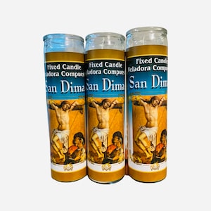 Puede incluir: Tres frascos de vidrio para velas con una imagen religiosa de un hombre en una cruz. La imagen está rodeada por un marco dorado y el texto "Fixed Candle Veladora Compues San Dima" está impreso en la parte frontal de cada frasco.