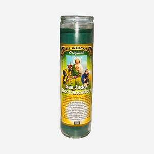 May include: A green glass candle with a label featuring the text "VELADORA Original San Judas Destrancadera" and an image of a saint. The candle is cylindrical and filled with green wax.