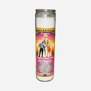May include: A tall glass candle filled with white wax. The label reads "VELADORA Original" and "Santa Muerte Desunión", with an image of a saint and two figures. This candle is intended for spiritual practices.