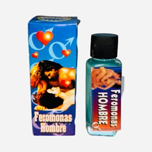 Könnte beinhalten: Eine blaue Schachtel mit einem Paar auf der Vorderseite und den Worten "Feromonas Hombre" unten. Eine kleine, durchsichtige Flasche mit schwarzem Verschluss und blauer Flüssigkeit im Inneren. Die Flasche trägt ein Etikett mit den Worten "Feromonas Hombre" darauf.