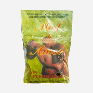 May include: A yellow and green package with a couple embracing on the front. The package is labeled "Miel de Amor con Feromonas" and "Bath of aromatic plants delightfully perfumed".