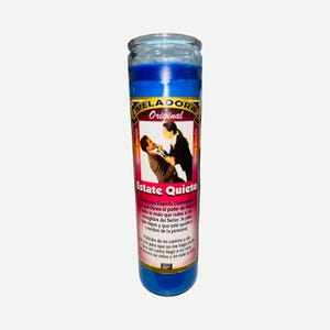 May include: A blue glass candle with a label featuring the text "VELADORA Original" and "Estate Quieto". The label depicts a person and a woman. The candle has a blue wax.