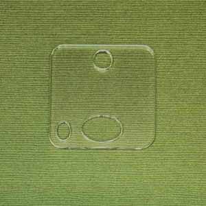 May include: A clear plastic template with three cut-out circles, one large and two small. The template is designed for crafting and DIY projects.