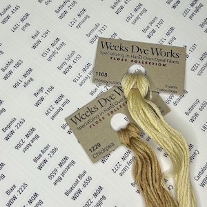 May include: A close-up of a collection of embroidery floss spools in various shades of yellow and brown. The spools are labeled with the brand name "Weeks Dye Works" and the color names "Honeysuckle", "Chickpea", and "Buttercup".