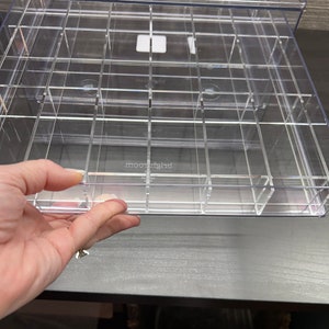 May include: A clear plastic storage box with multiple compartments. The box is divided into rows and columns, creating individual spaces for storing small items. The box is labeled "moonlight" on the front.