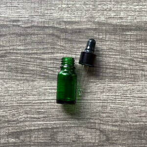 May include: A green glass bottle with a black dropper top. The bottle is empty and the dropper is separate.