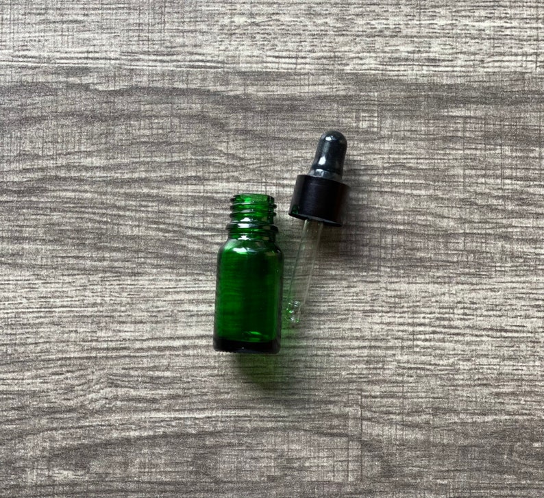 May include: A green glass bottle with a black dropper top. The bottle is empty and the dropper is separate.