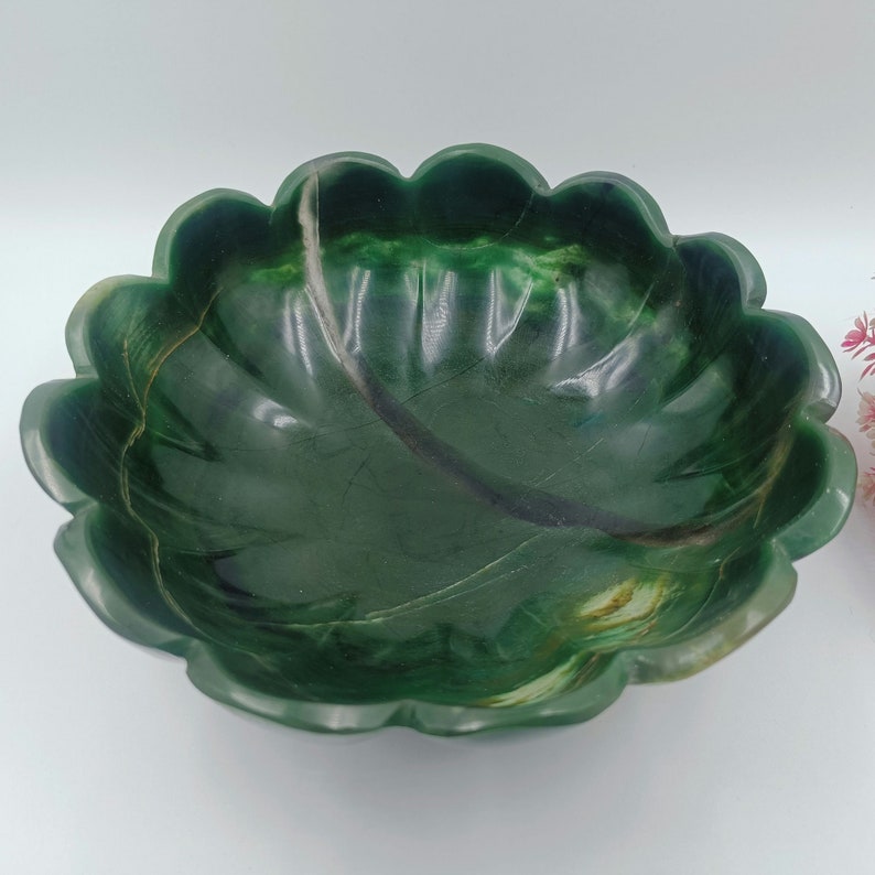May include: A green jade bowl with a scalloped edge and a leaf-like design. The bowl is made of natural stone and has a smooth, polished finish.