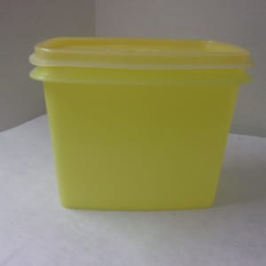 Puede incluir: Un recipiente de almacenamiento rectangular de plástico amarillo con tapa. El recipiente está hecho de plástico translúcido y tiene una superficie lisa.