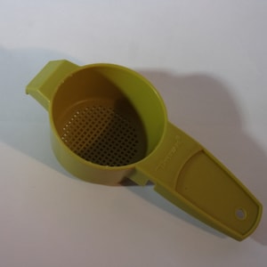 以下が含まれることがあります： ハンドルとメッシュの底を持つ黄色のプラスチック製の茶こし。こし器には側面に「タッパーウェア」と印刷されています。