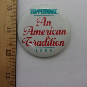 May include: White round button with the text "Tupperware" in teal blue, "An American Tradition" in red, and "1986" in teal blue.