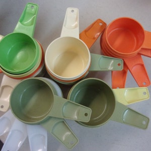 May include: A set of vintage measuring cups in various colours, including green, orange, yellow, and white. The cups are made of plastic and have a handle on each side.