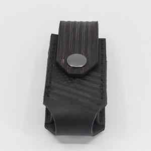 May include: A black leather belt pouch featuring a debossed American flag pattern on the front flap. The rectangular case is secured with a single silver-toned metal snap button closure and has visible black stitching along the edges.