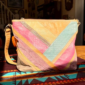 May include: A colorful shoulder bag with a patchwork design. The bag features a variety of textures and colors, including pink, orange, green, and brown. The bag has a long, adjustable strap and a zipper closure.