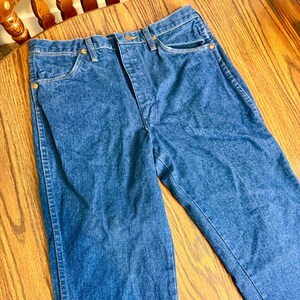 May include: A pair of blue denim jeans with a classic five-pocket design. The jeans have a button and zipper closure, and copper-colored rivets. The fabric appears to be a medium-wash denim, with a slightly faded look.