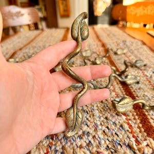 May include: A set of antique brass leaf-shaped drawer pulls. Each pull features a curved stem with two detailed leaves. The brass has a warm, aged patina. Several pulls are visible, suggesting a set for multiple drawers.