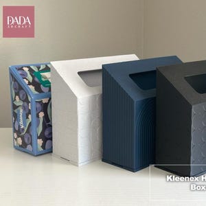 May include: Four Kleenex hand towel box covers in a row. The first is patterned with blue and green floral designs. The second is white with a subtle embossed pattern. The third is navy blue with vertical lines. The fourth is black with a repeating pattern.