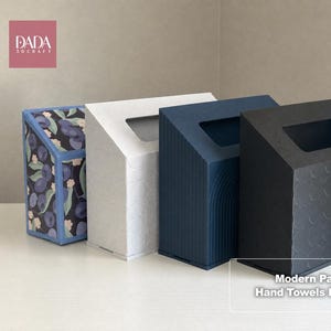 Könnte beinhalten: Vier rechteckige Handtuchbox-Abdeckungen mit schrägen Oberseiten und rechteckigen Öffnungen. Eine zeigt ein blau-schwarzes Blaubeermuster, während die anderen einfarbig weiß, marineblau mit vertikalen Linien und schwarz mit kreisförmigem Muster sind.