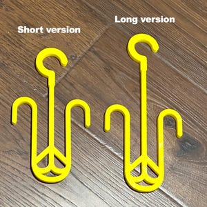 Puede incluir: Dos perchas de pl&aacute;stico amarillo con un dise&ntilde;o de signo de paz. La percha de la izquierda es m&aacute;s corta que la percha de la derecha.