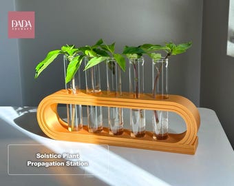 May include: A mustard yellow, oval-shaped 3D-printed plant propagation station featuring five clear glass test tubes. Each tube holds a green plant cutting. The text DADA 3DCRAFT and Solstice Plant Propagation Station are visible.