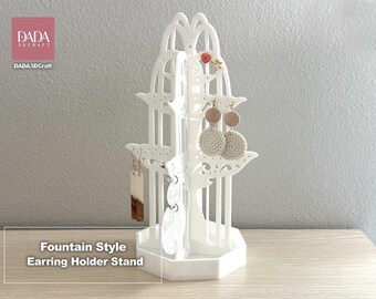 May include: A white fountain style earring holder stand with a hexagonal base and vertical tiered branches for displaying jewelry. The stand features intricate cutouts and holds various pairs of earrings. Text on the image reads DADA 3DCRAFT.