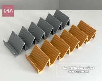 May include: Two sets of tiered organizers, one in dark gray and one in mustard yellow, each featuring a zigzag, accordion-style design with multiple slots for holding items. The text DADA 3DCRAFT and Cash & Business Card Tray Organizer are visible.