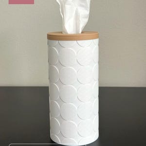 K&ouml;nnte beinhalten: Eine wei&szlig;e zylindrische Taschentuchbox-Abdeckung mit einem erhabenen kreisf&ouml;rmigen Muster auf der Au&szlig;enseite und einem latte-braunen Deckel. Das Produkt ist mit DADA 3D CRAFT beschriftet und als Round Cylinder Tissue Box Cover, White Cover, Latte Brown Lid gekennzeichnet.