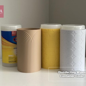 May include: A set of cylindrical disinfecting wipes container covers in beige, yellow, and light gray. The beige cover features vertical arched lines, the yellow cover has a geometric grid pattern, and the light gray cover has a circular pattern.
