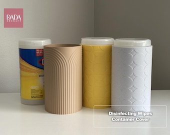 May include: A cylindrical disinfecting wipes container next to three decorative covers. One cover is beige with vertical arched lines, one is yellow with a geometric semi-circle pattern, and one is light gray with a repeating circle design.