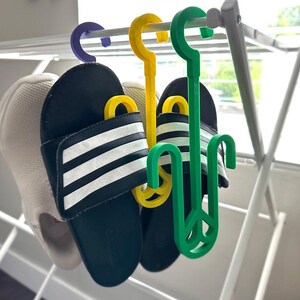 Puede incluir: Dos pares de sandalias rayadas en blanco y negro colgadas de un tendedero blanco con ganchos de pl&aacute;stico verde y amarillo.