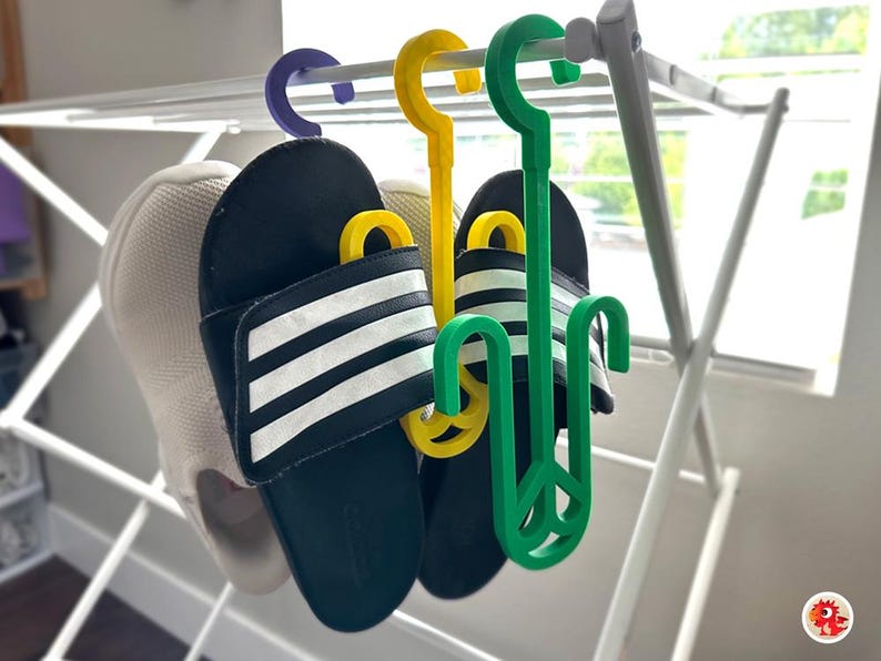 Puede incluir: Dos pares de sandalias rayadas en blanco y negro colgadas de un tendedero blanco con ganchos de pl&aacute;stico verde y amarillo.