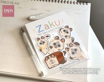 May include: A set of five die-cut stickers featuring a cartoon Lynx point Siamese cat named Zaku. The stickers display various expressions and poses of the cat, including one inside a piece of bread. The text reads Zaku The Lynx point Siamese.