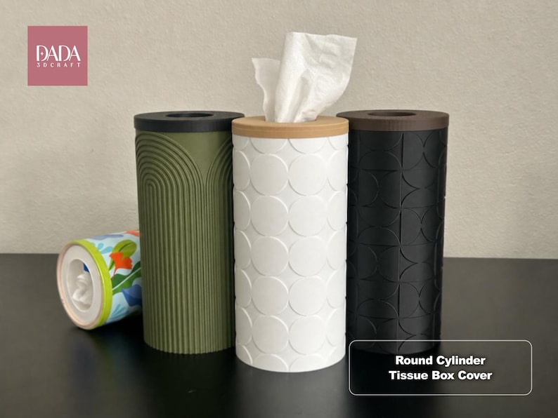 K&ouml;nnte beinhalten: Vier zylindrische Taschentuchbox-Abdeckungen. Eine ist olivgr&uuml;n mit Bogenmuster, eine wei&szlig; mit Kreismuster, eine schwarz mit geometrischem Muster und eine liegt mit Blumenmuster. Text: DADA 3DCRAFT und Round Cylinder Tissue Box Cover.