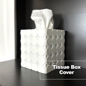 May include: White tissue box cover with a circular pattern. The cover is made of a hard material and has a modern design. The text "Tissue Box Cover" is printed on the bottom of the image.