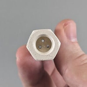 May include: A white ceramic hexagonal diffuser with three small holes in the centre.