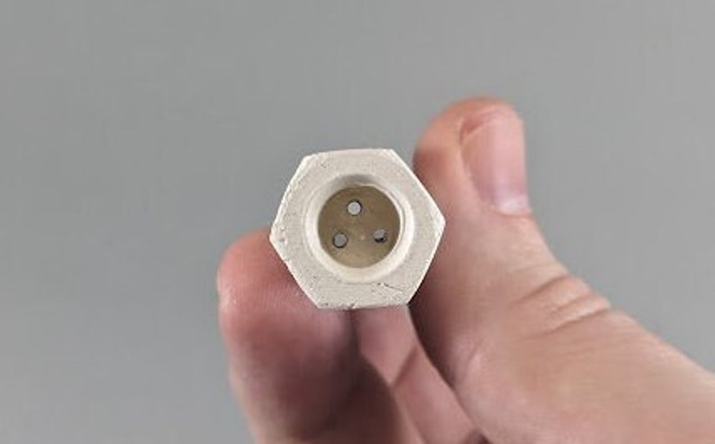May include: A white ceramic hexagonal diffuser with three small holes in the centre.