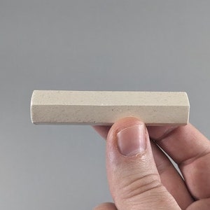May include: A close-up of a white chalk stick, held in a hand. The chalk stick is rectangular in shape and has a rough texture.