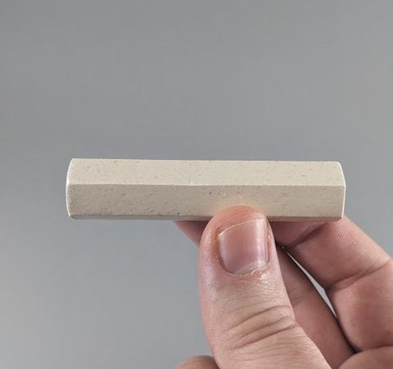 May include: A close-up of a white chalk stick, held in a hand. The chalk stick is rectangular in shape and has a rough texture.