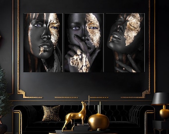 May include: Three black and gold abstract art prints featuring close-up portraits of faces with gold leaf accents. The prints are framed and displayed on a black wall above a black velvet sofa.
