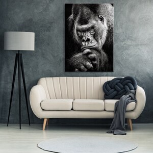May include: Black and white photograph of a gorilla looking directly at the camera. The gorilla is sitting with its chin resting on its hand. The photo is printed on canvas and framed.